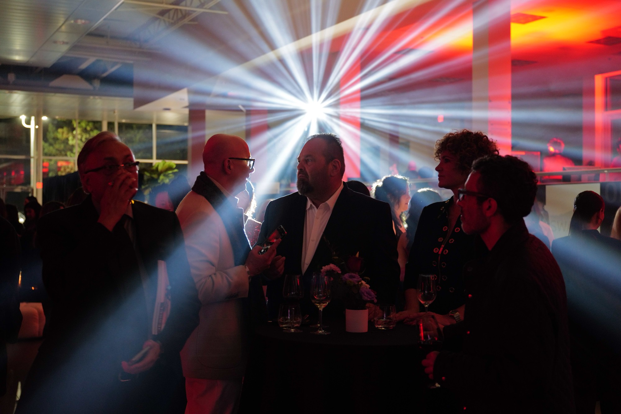 Guests in conversation beneath dramatic white beams and red event lighting
