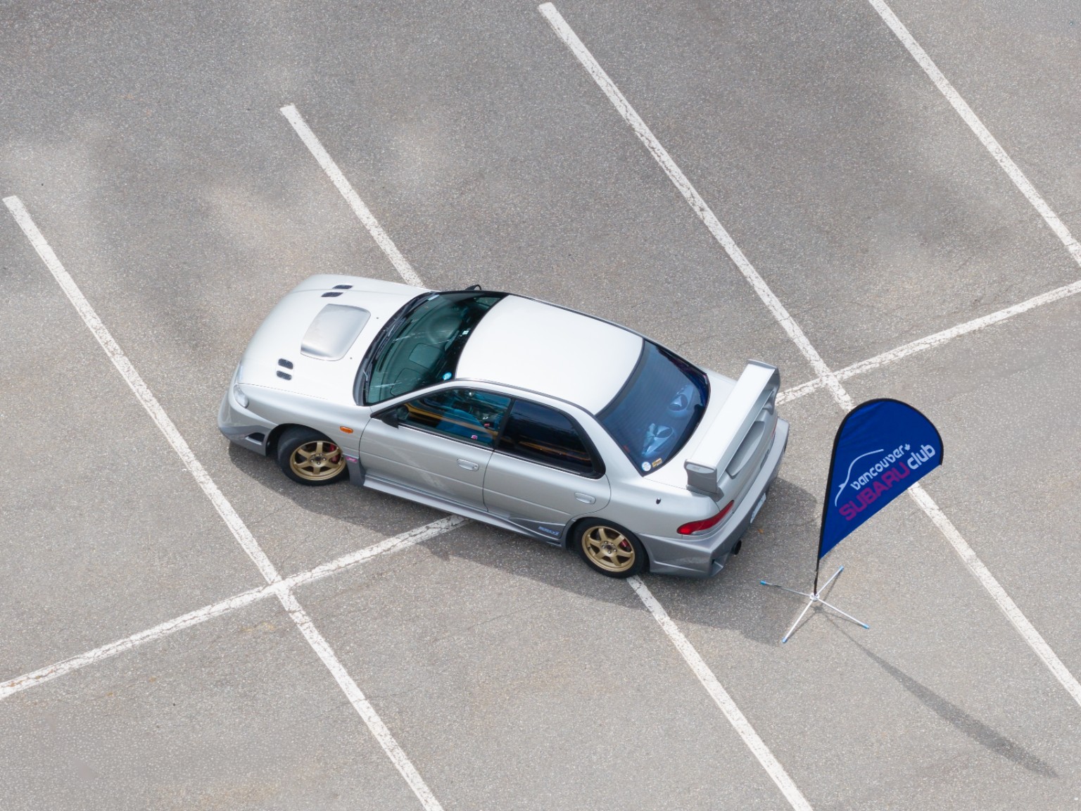 Overhead view of a silver Subaru beside a Vancouver Subaru Club flag