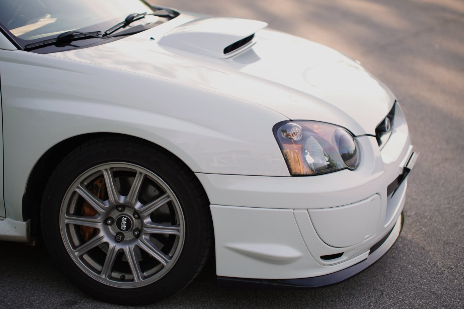Front quarter of a white Subaru showing its hood scoop, headlight and wheel
